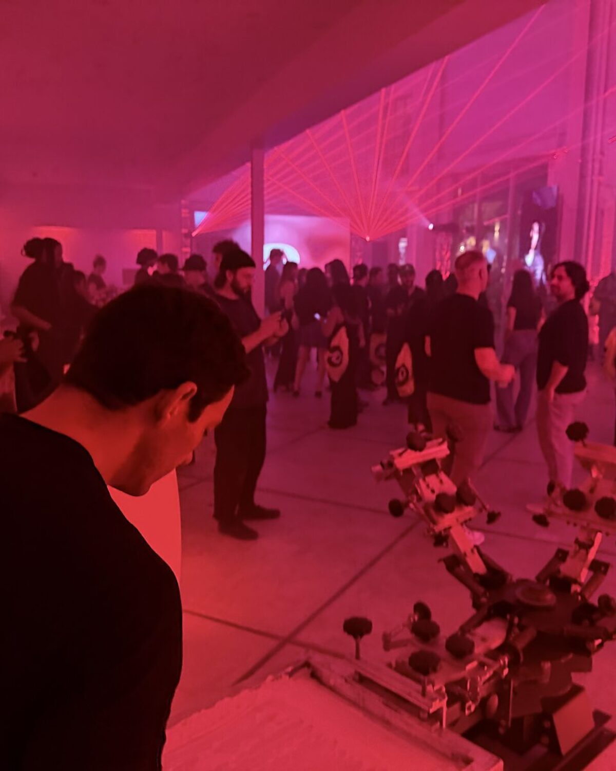 A nighttime event under magenta laser-fan lighting with a crowd and a live screen-print carousel in the foreground